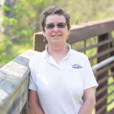 Woman standing along fence in front of trees