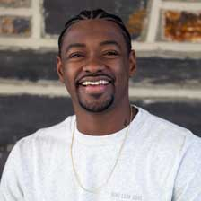 Chaz Dawson stands in front of a brick wall and smiles without glasses or contact