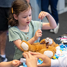 a young girl puts the tube in a fake syringe for her teddy bear