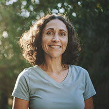 Woman stands outside in front of trees while smiling