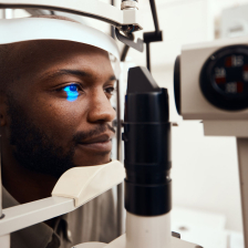 Man with his head on a holder looking into an eye machine that is flashing light 