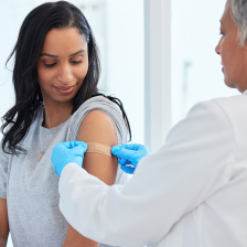 a woman looks at her shoulder while the doctor puts a bandage on after giving a flu shot