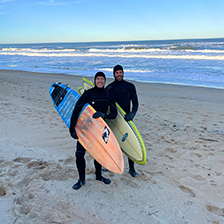 Zach and Josh stand on the beach with surf boards