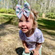 Child wearing bow on head, leaning into camera and laughing