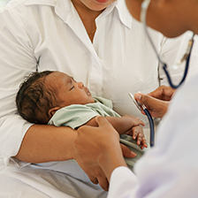 A mother holds her baby while the doctor holds a stethescope to its chest