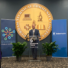 Duke Health CEO Dr. Craig Albanese speaks at a podium surrounded by banners from Duke Health, Durham Public Schools and Durham Tech