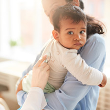 a mother holds her baby while the doctor holds up a stethoscope to their back