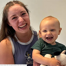 Young woman holds a toddler. Both are laughing.