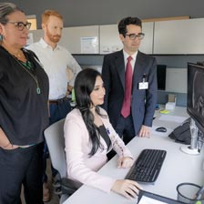 a panel of doctors stands and looks at a computer