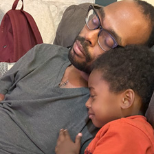 Child holds man while in chair. Man has heart transplant scar.