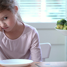 Child looks warily at a plate of broccoli