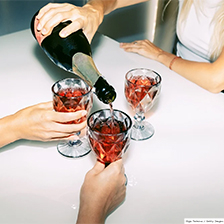 Three people share drinks at a table. One pours from a bottle.