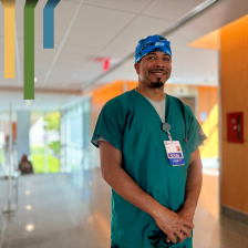 Kelvin smiles in green scrubs and a scrub hat in a Duke University Hospital hallway.
