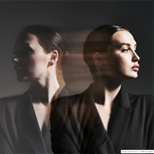 A woman looks passively to the right while her reflection looks left