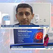 Dr. Nishant Shah talking on TV w/ Heart Attack warning symptoms graphic and reporter from WRAL present