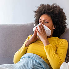 A woman sits on a couch and wipes her nose with a tissue
