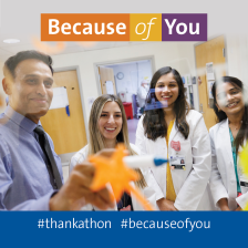 A group of trainee doctors in white coats smile at the camera and gesture at a whiteboard.