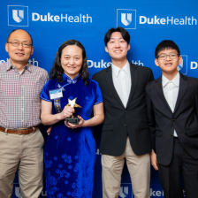 Haiyan and her family smile for a photo at a gala honoring her with a Friends of Nursing Award. They are standing in front of a backdrop with the Duke Health logo.