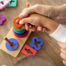 One hand guides another using building blocks on a peg board