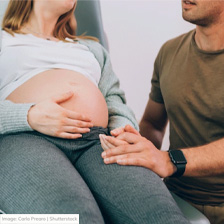 Pregnant woman sits on a medical bed while a man holds her hand.