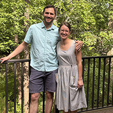 Two people stand in front of a wooded setting