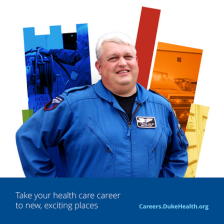Cory smiles in a blue Duke Life Flight suit with a colorful Duke shield behind him. 