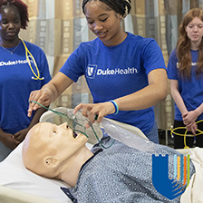 A student puts a mask on a medical mannequin while two other students observe