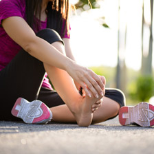 A woman sits on the ground after a run holding her foot