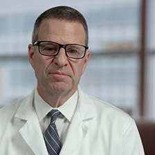 Dr. Tom Owens speaks in front of a lighted background, weaering a shirt tie and lab coat