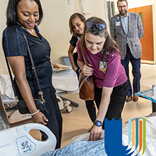Students approach a medical mannequin in a hospital setting