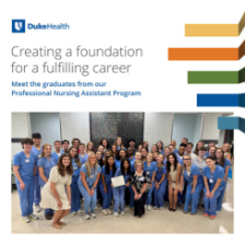 Group of Duke Health professional nursing assistant graduates posing together in blue scrubs, smiling in a hospital lobby.