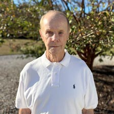 Stanley stands outside in front of a tree smiling slightly.