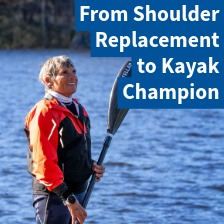 Vicki Reynolds holds her kayak paddle next to a lake and smiles