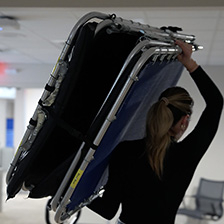 Woman carries a folded cot across a room