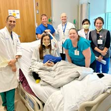 Emily sits in her hospital bed with her transplant team surrounding her