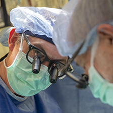 Dr. Turek looks into the camera, wearing magnifiers on his glasses while wearing protective gear in a surgical suite