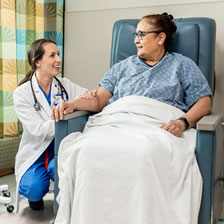 A doctor kneels next to a patient in a chair
