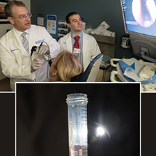 Dr. Bradley Goldstein and Vincent D'Anniballe are examining a patient's nose using medical equipment. They're looking at a monitor displaying an internal view of the nose. Below, there is a close-up of a hand holding a test tube with a pink liquid inside with a swab, illuminated by a light source.