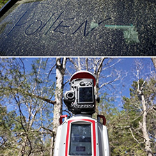 A window with yellow pollen has the word pollen written in the pollen, above a robotic scanner, standing in a field of trees