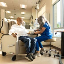 A man sits in a chair while a nurse administers medication through IV