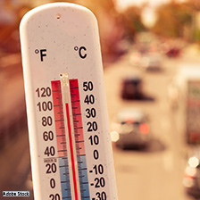 A thermometer showing heat in the 100 degree range over a street scene