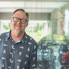 Man in a shirt with lobster images leans into a mirror, showing a duplicate, reversed image of himself.